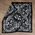 Black scarf with white floral pattern and logo on a wooden surface