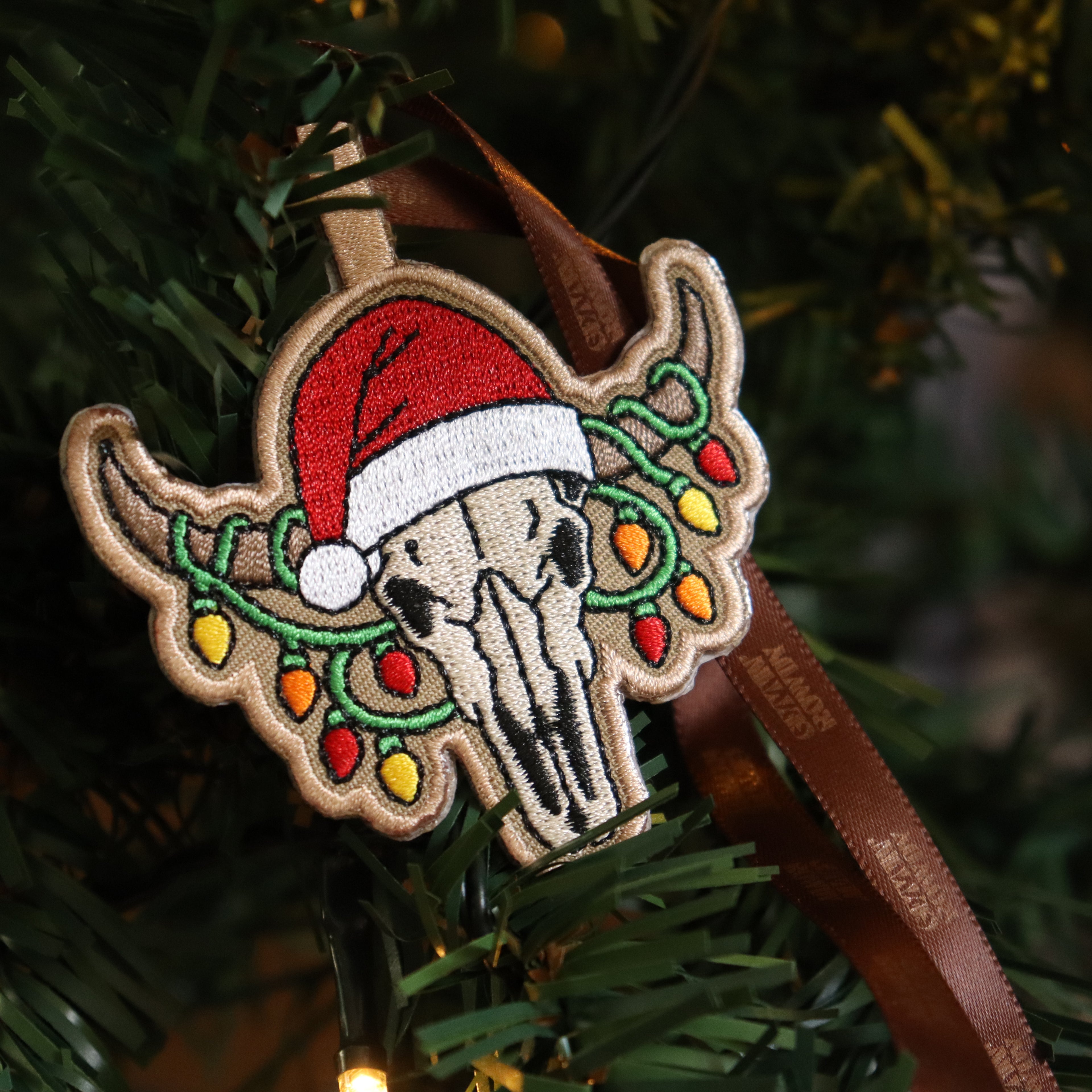 Decorative Christmas ornament with a longhorn skull wearing a Santa hat and surrounded by lights on a tree.