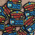 Collection of 'Whiskey Bent and Neon Bound' patches on a wooden surface