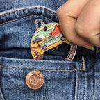 Hand holding a colorful keychain with a truck design against a denim background